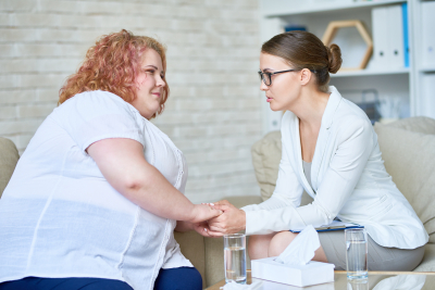 Female psychiatrist offering psychological support to obese young woman holding hands
